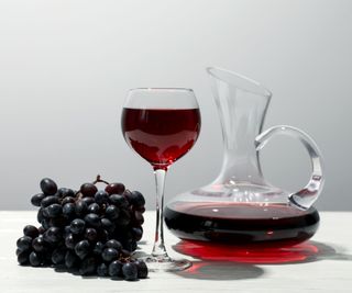 wine decanter on a white surface with grapes and a wine glass