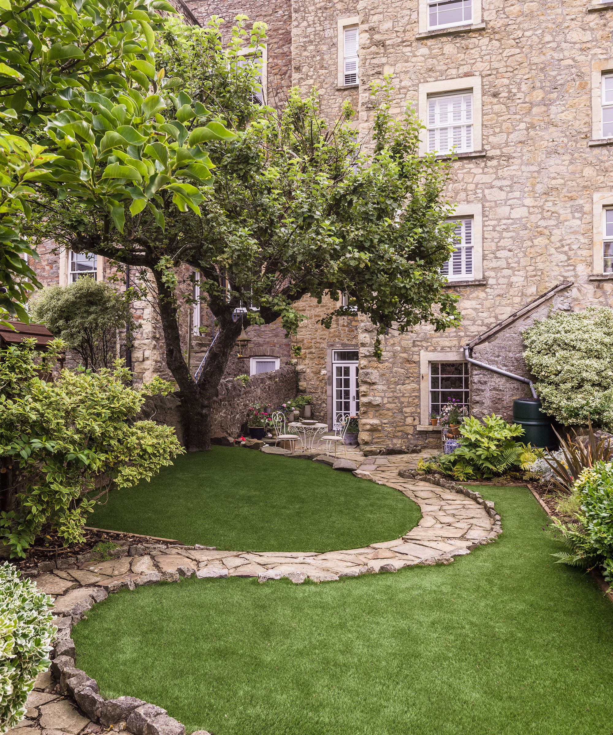 A garden with a curved pathway leading up to the house next to a tree