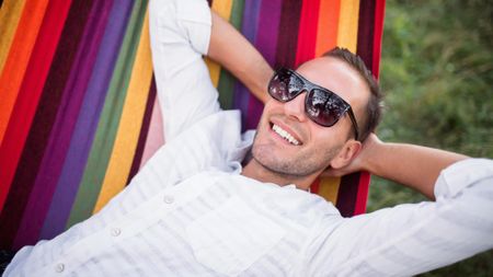 Young man in sunglasses smiling and leaning back in a colourful hammock