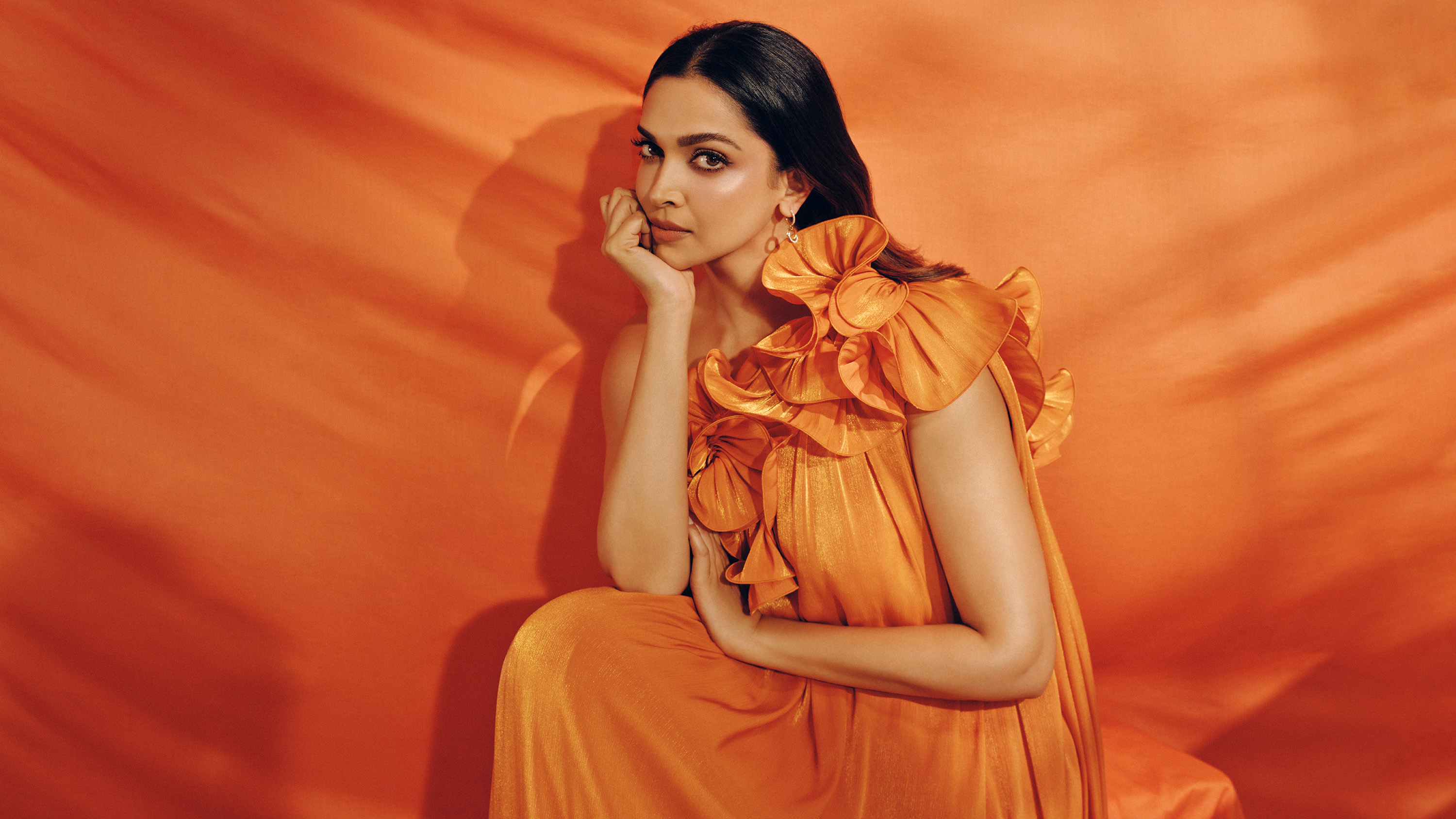deepika padukone wears a silk orange dress and poses with her hand under her chin in a marie claire photo shoot