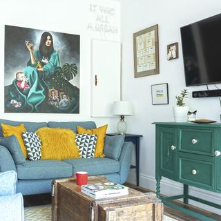 living area with white wall and blue television and green chest adn television and painting