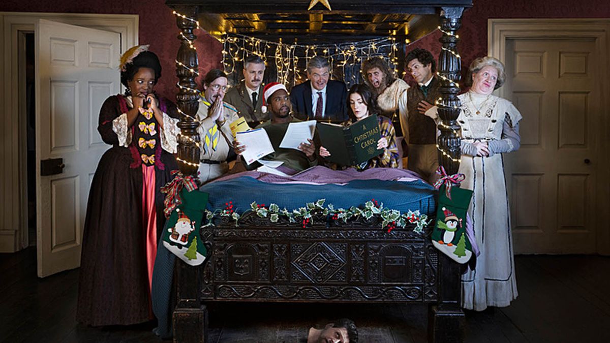 Ghosts Christmas special 2023 gather around with Mike wearing a festive hat and Alison reading A Christmas carol