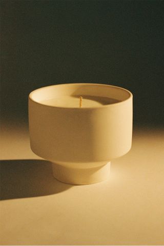 Uniform fragrance candle in white circular holder against black background