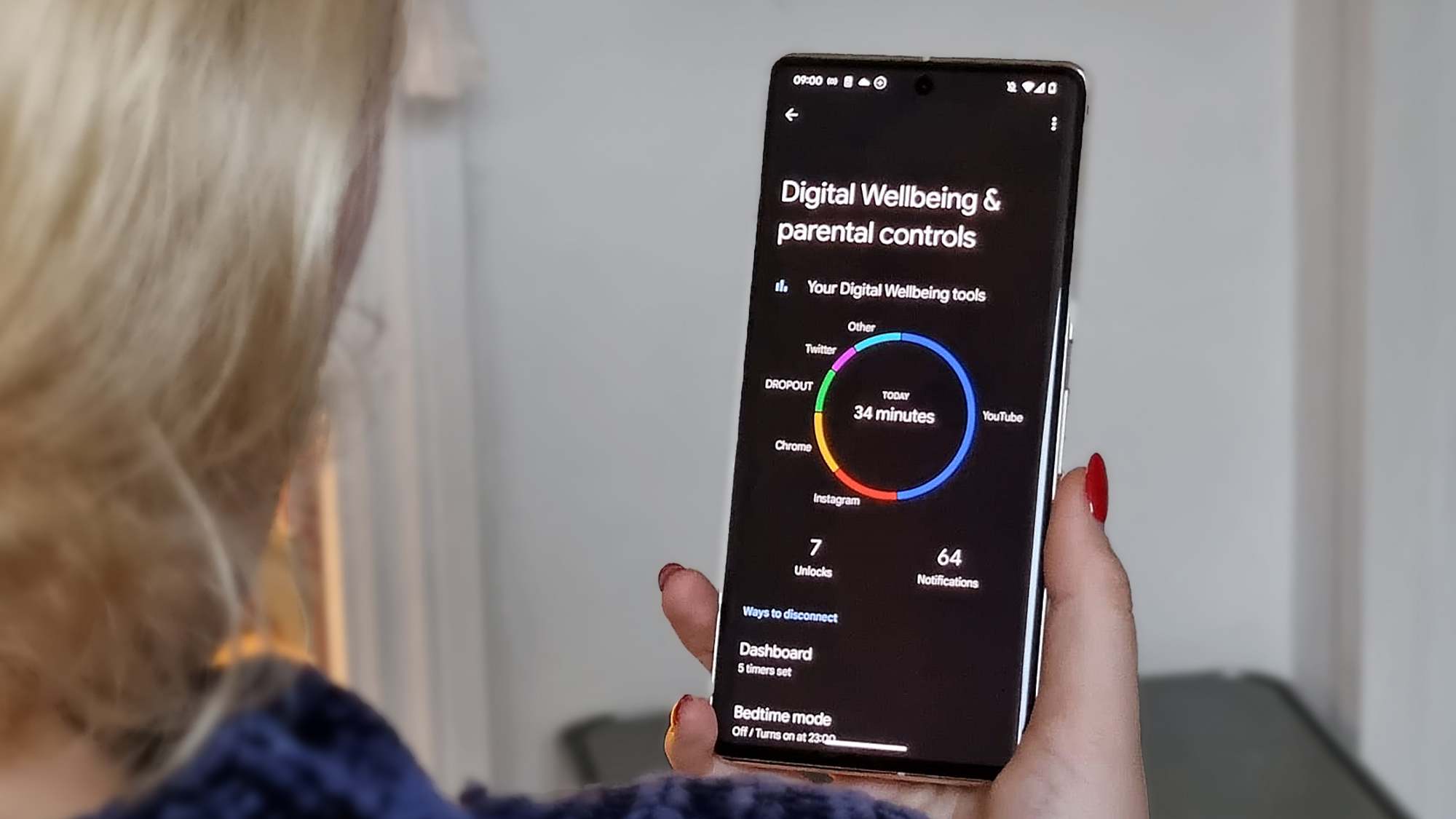 Over-the-shoulder shot of a woman holding a Google Pixel 7 Pro and looking at Android's Digital Wellbeing dashboard