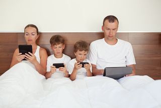 family on electronic devices in bed