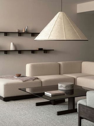 A warm beige living room with a beige modular sofa, a black glossy coffee table, and an oversized paper lantern.