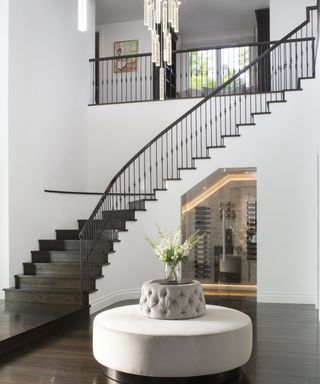 A white entrance hall with a black curved staircase and wine cellar