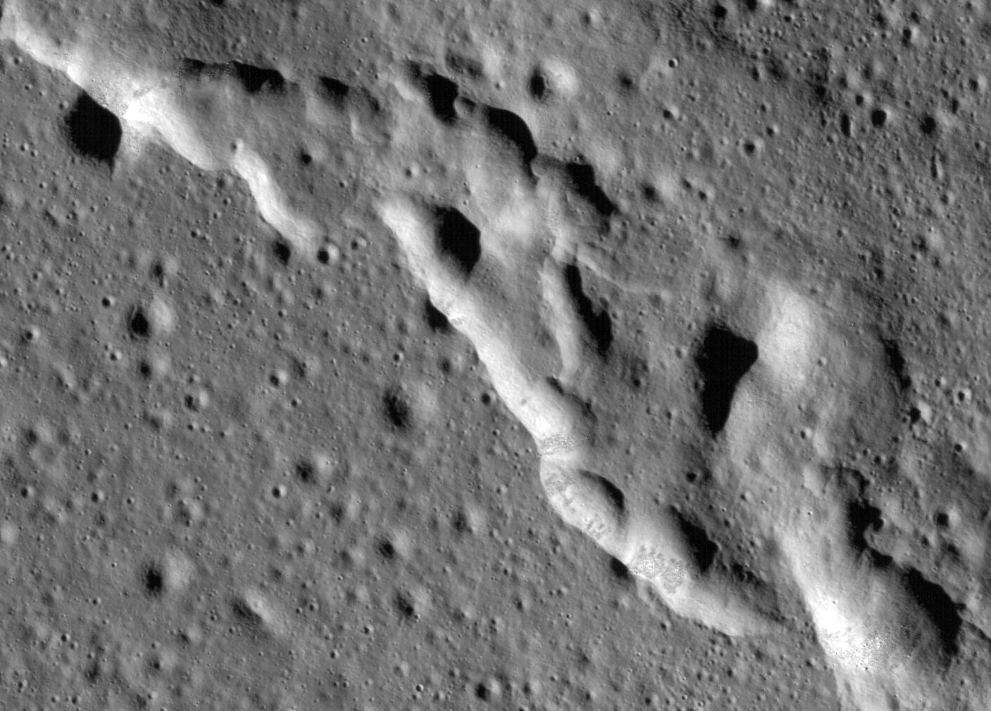 looking down at a grey landscape pockmarked with tiny craters and a hillside cut diagonally from the top left.