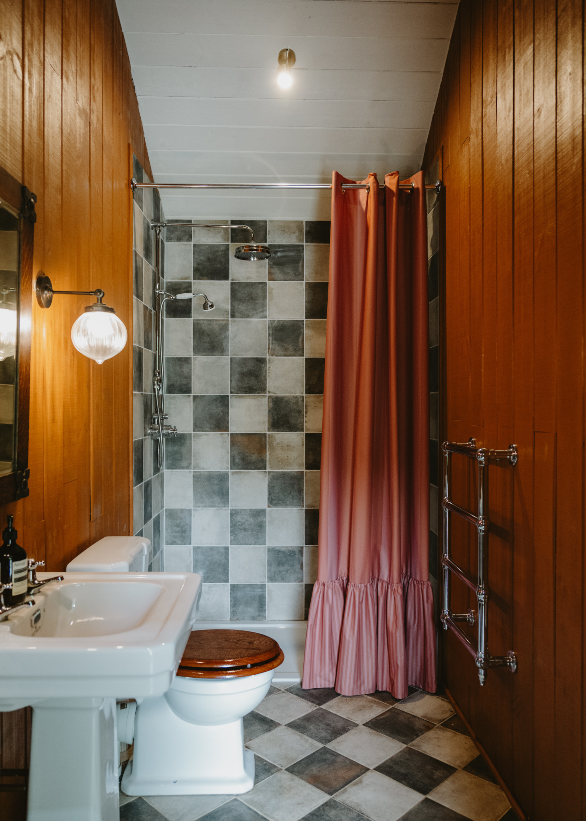 wooden clad bathroom with checkerboard tiles and a frilly shower curtain