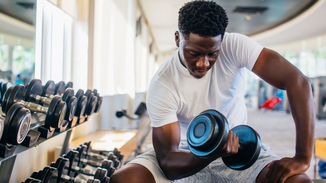 Man performing dumbbell curls in gym trying to build muscle