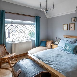 Blue bedroom with double bed with blue linen, blue curtains and rocking chair.