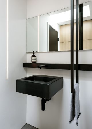 A bathroom with black sink, shelf and LED strip light