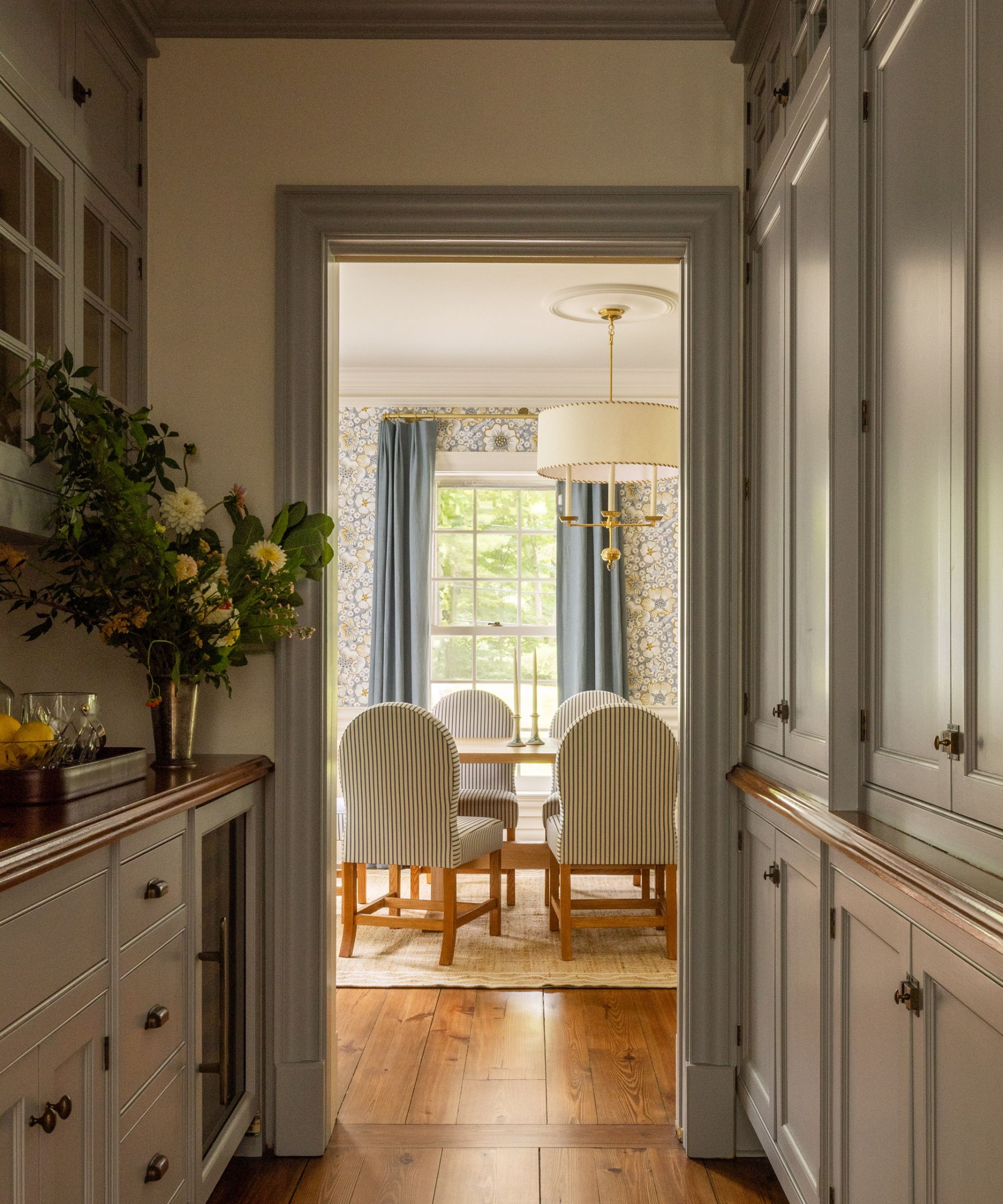 Hallway with cabinets looking into dining room with blue floral wallpaper and striped blue dining chairs