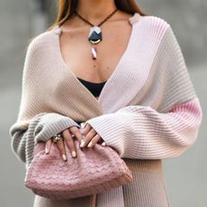 woman wearing long pastel knit, holding pink bag with butter yellow nails