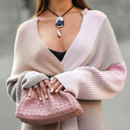 woman wearing long pastel knit, holding pink bag with butter yellow nails