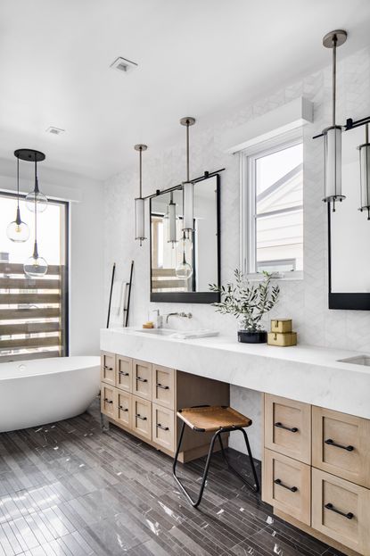 white bathroom with wooden vanity, double sinks, double mirrors, grey floor tiles, white tub