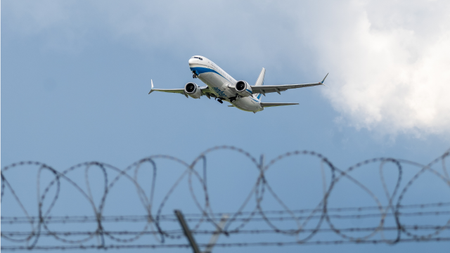 a Boeing 737 taking off behind an airport security fence