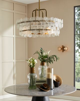 An entryway with a round table, a large glass chandelier, and an exposed bulb wall light