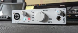 An Arturia MiniFuse 1 audio interface on a desktop with various musical equipment in the background