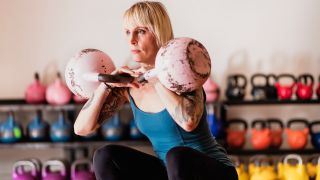 Woman performs double kettlebell squat