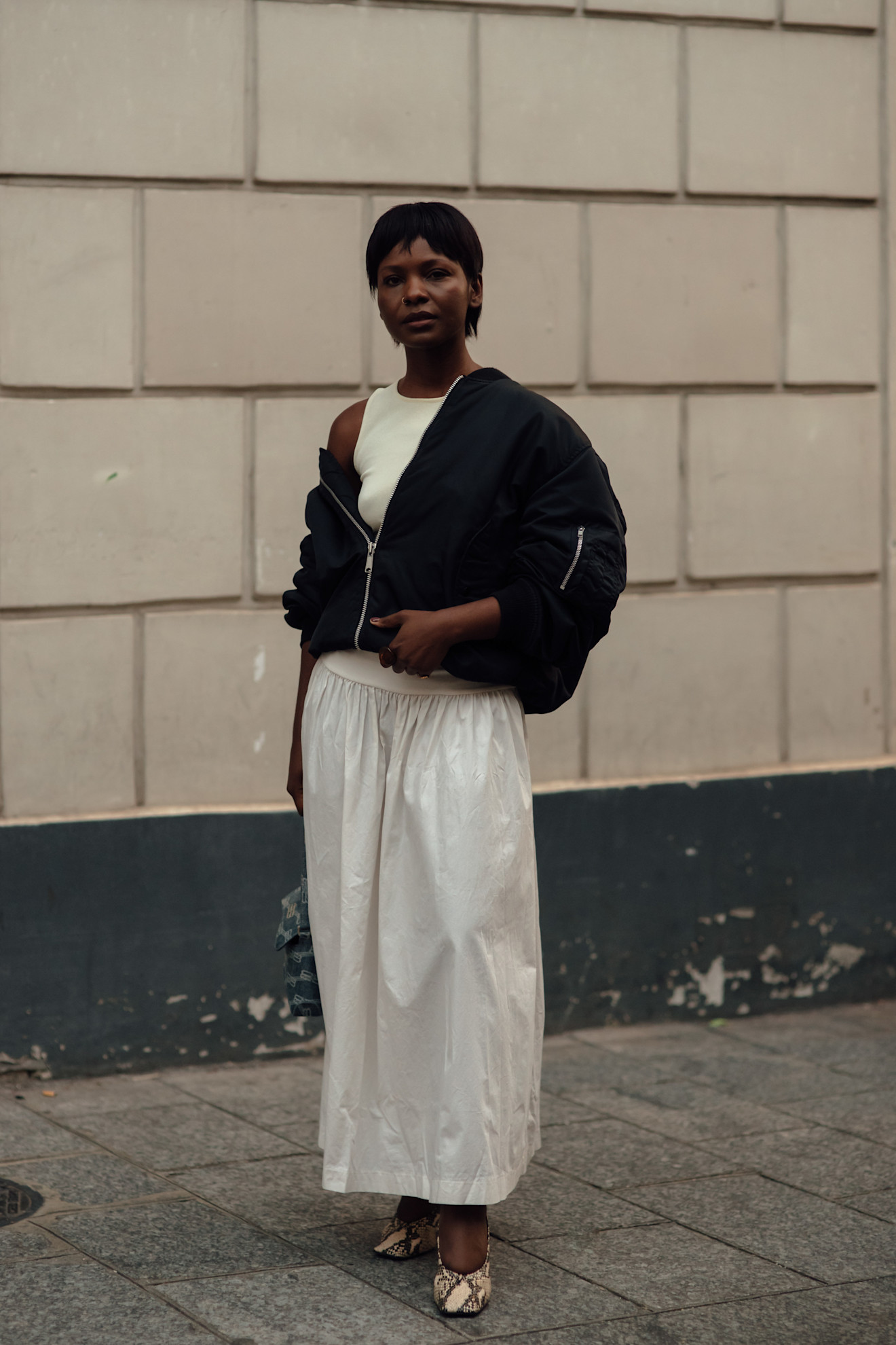 woman wearing bomber jacket, white skirt, and flats
