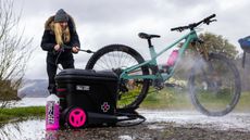 A customer using a Muc-Off pressure washer on their bike with branded accessories in the foreground