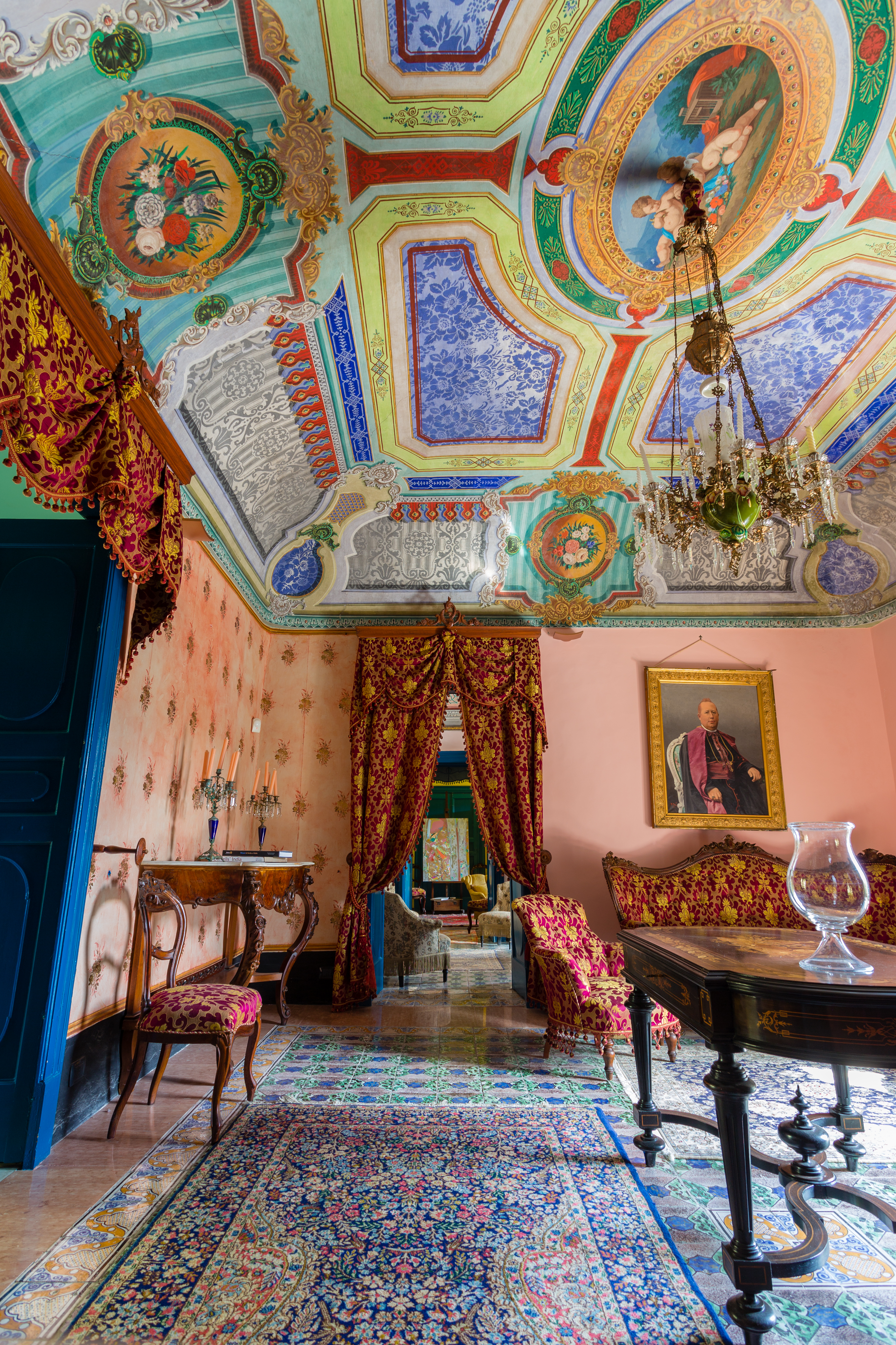 Peach coloured room with antique red and gold furniture and very colourful fresco ceiling