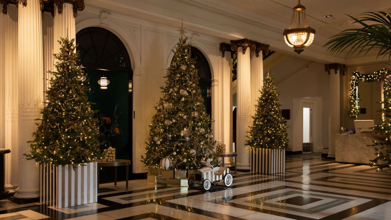 Three large Christmas trees placed in a hotel lobby with a view of the trees skirting and decor pieces finely presenting each Christmas tree. 