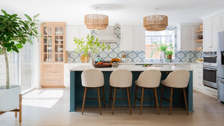 A white kitchen with blue island, taupe bar chairs, white and blue patterned tiles and wooden glass-fronted cabinet