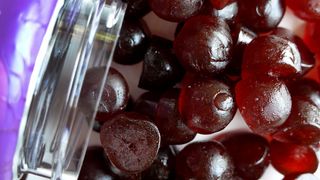 close-up photo of dark red melatonin gummies spilling out of a plastic jar onto a table