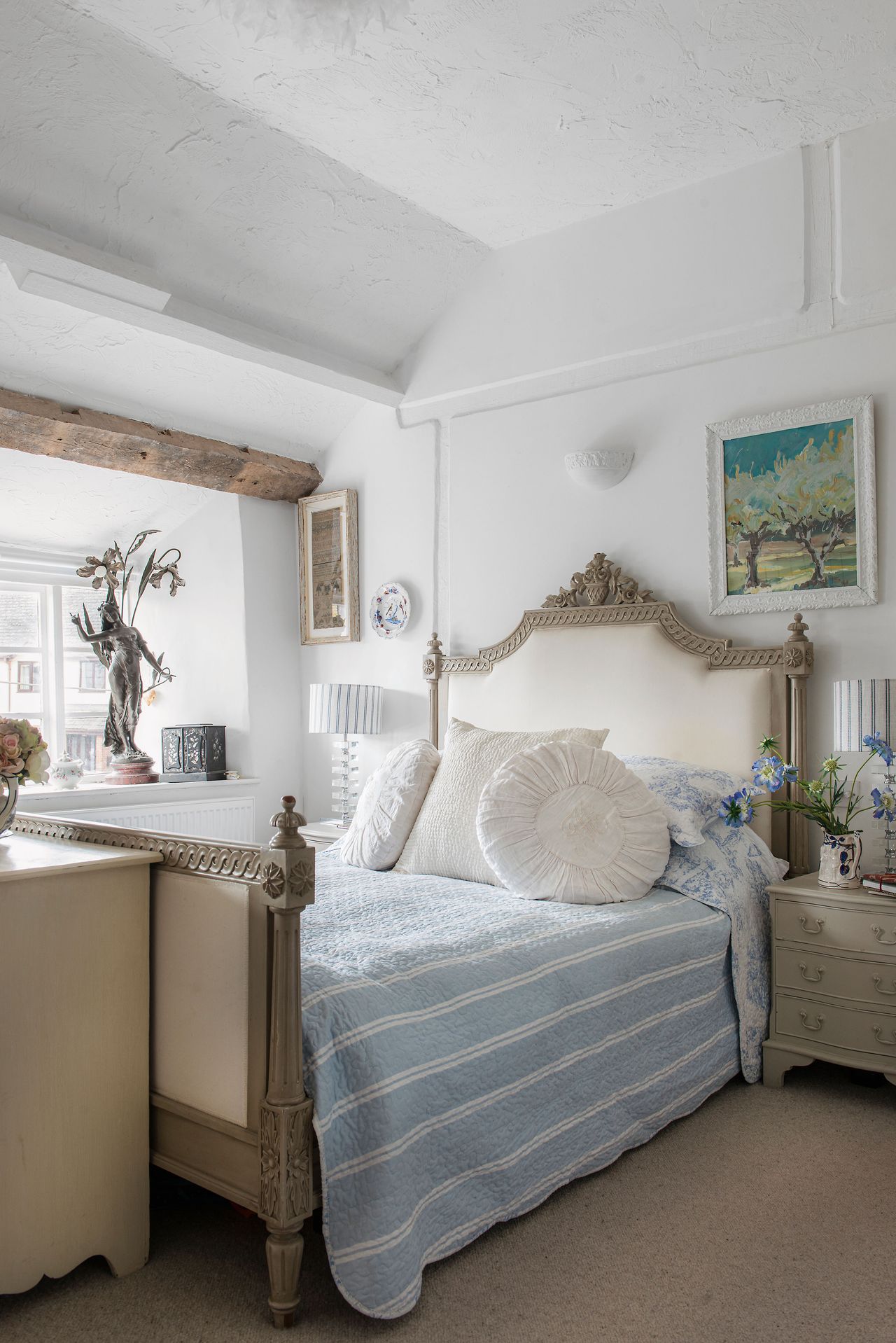 bedroom with ornate french-style upholstered bed and striped bed cover with round pillows and white walls