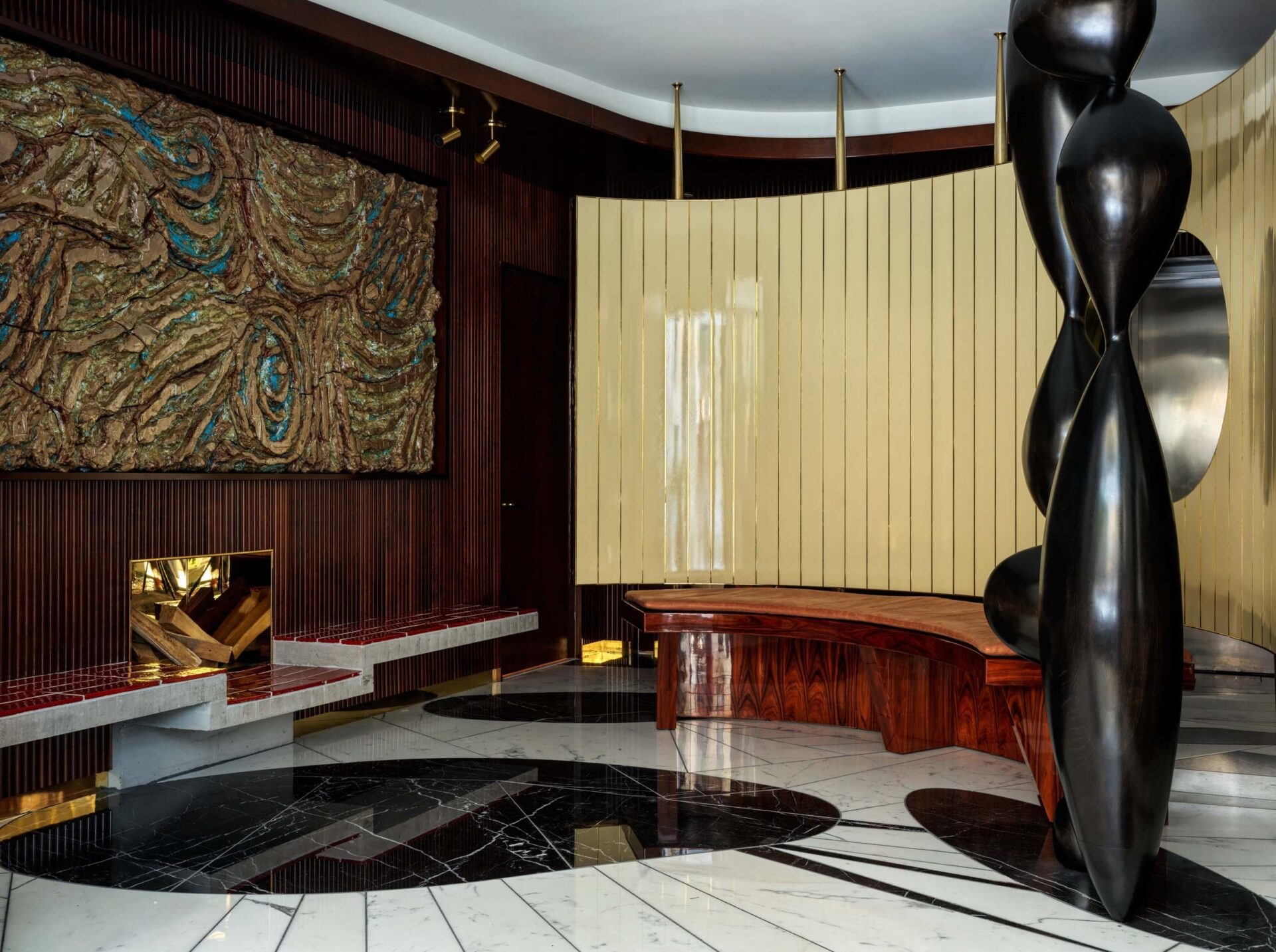 A glamorous, 1970s-inspired New York hotel boasts rooms defined by sleek, shiny surfaces, an earthy color palette, sculptural chandeliers and artwork accents, and textural details.