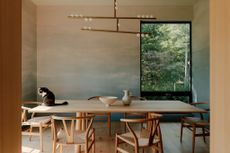 A designer home with a wooden table, colourful wallpaper and a big window leading into a green garden. The Wishbone Chairs are designed by Hans Wegner. 