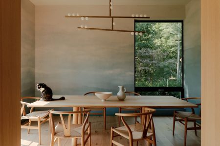 A designer home with a wooden table, colourful wallpaper and a big window leading into a green garden. The Wishbone Chairs are designed by Hans Wegner. 