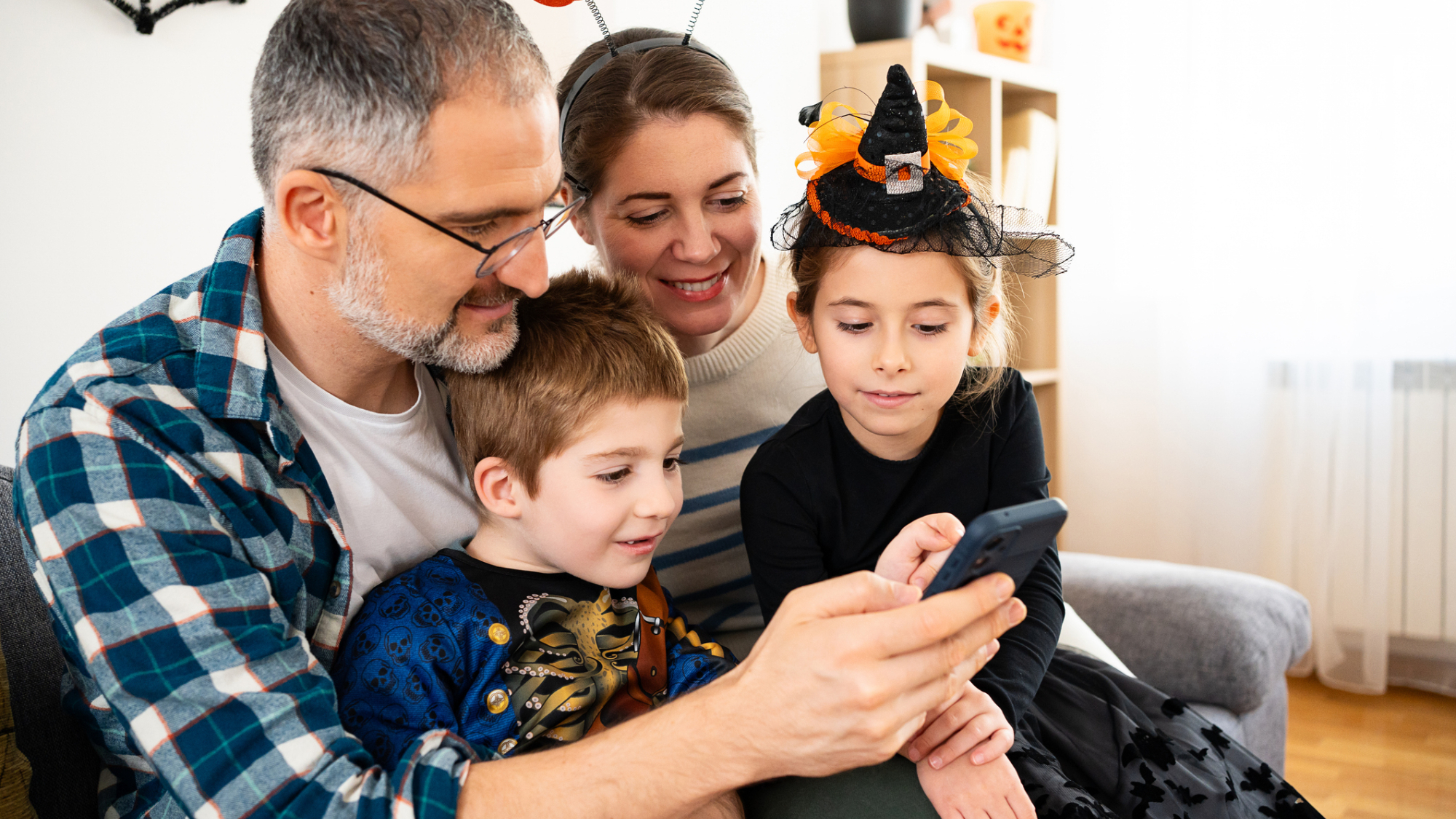 A family looking at a phone, sat on a couch, dressed for Halloween