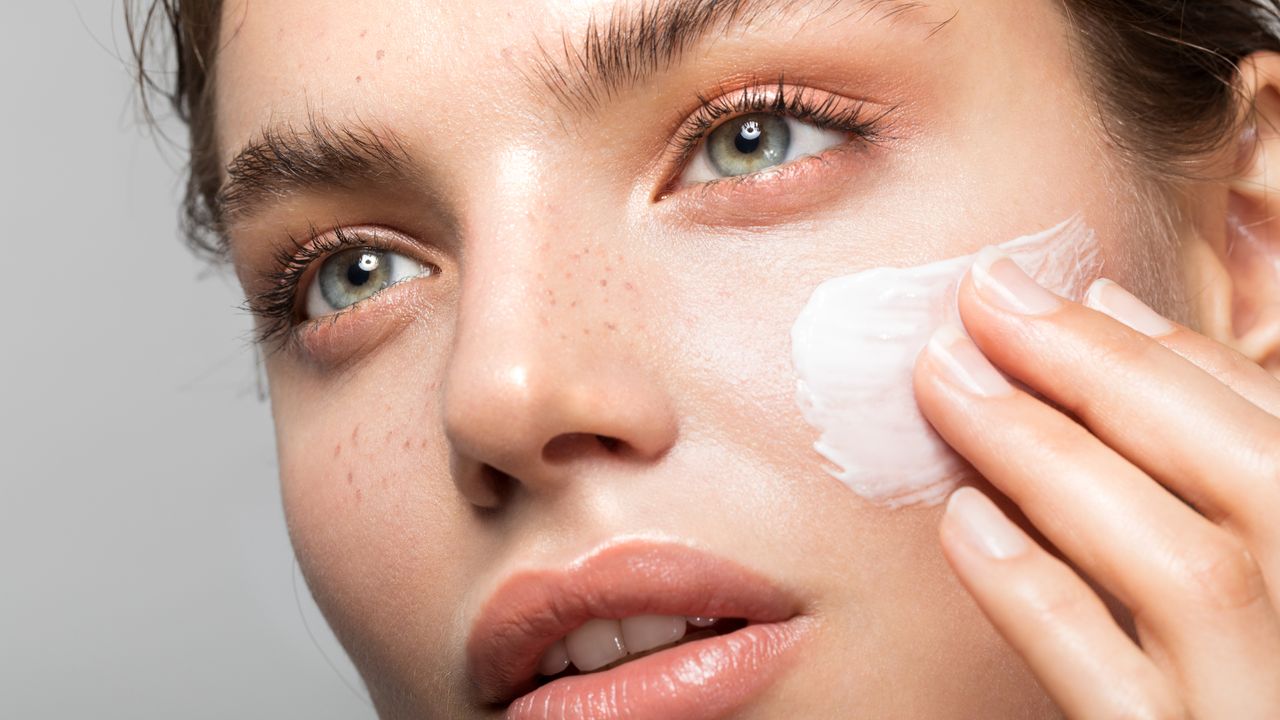 Young woman applying skincare to her face with bright glowy skin