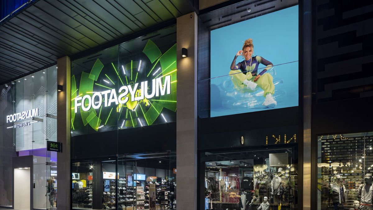 The high-brightness Philips LED display shines outside a UK retail store with the green logo of a shoe store and a smiling woman in sneakers.