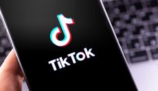 The TikTok logo displayed on a smartphone screen with a computer keyboard in the background.