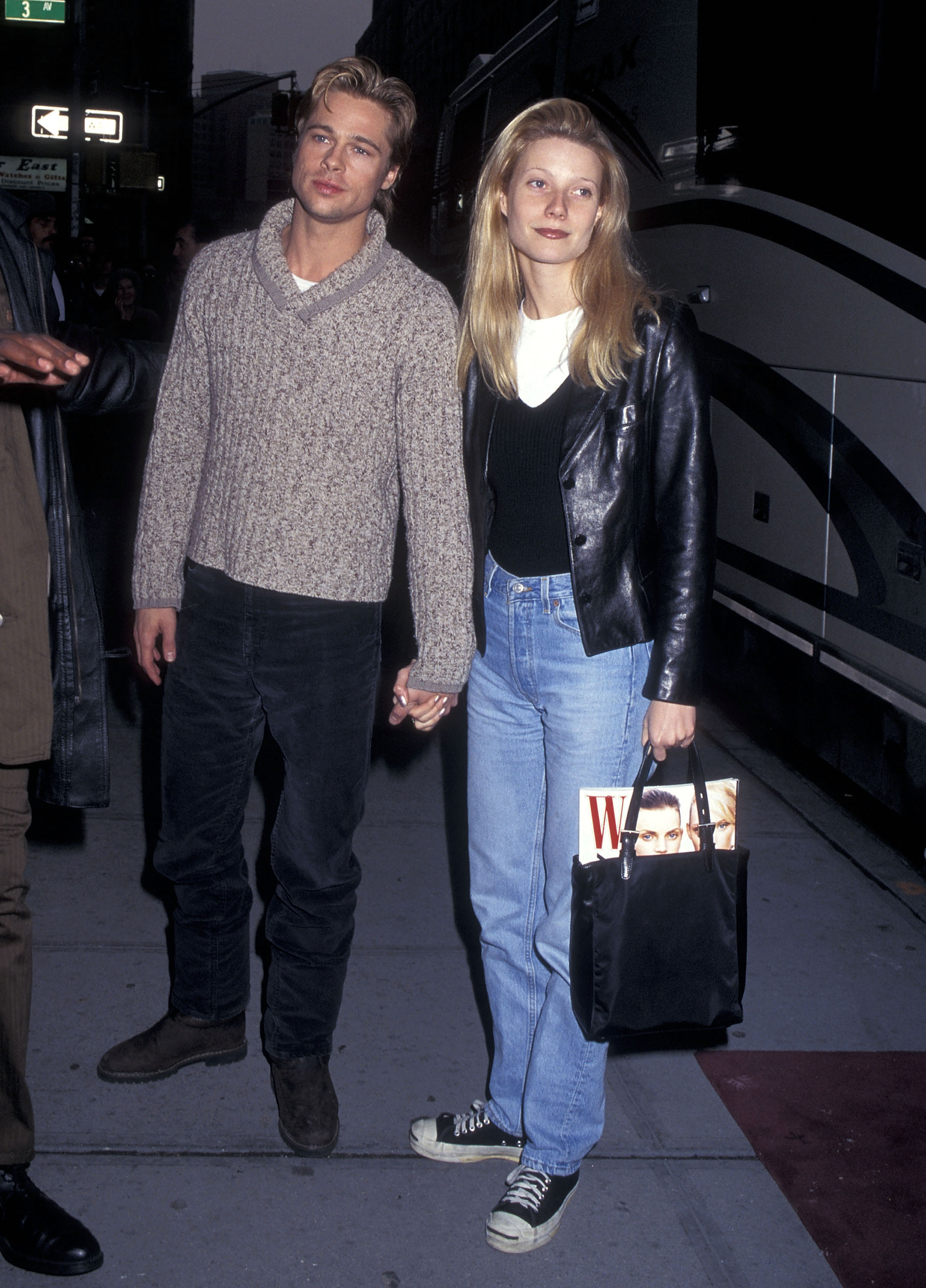 Gwyneth Paltrow wears a 90s autumn jeans outfit. On set of The Devil's Own in New York, 1996 she wears a blue denim jean, black v neck jumper, white t-shirt. She finishes the look with chuck taylors and a black bag with a issue of W hanging out. This image was recently taken from Getty.