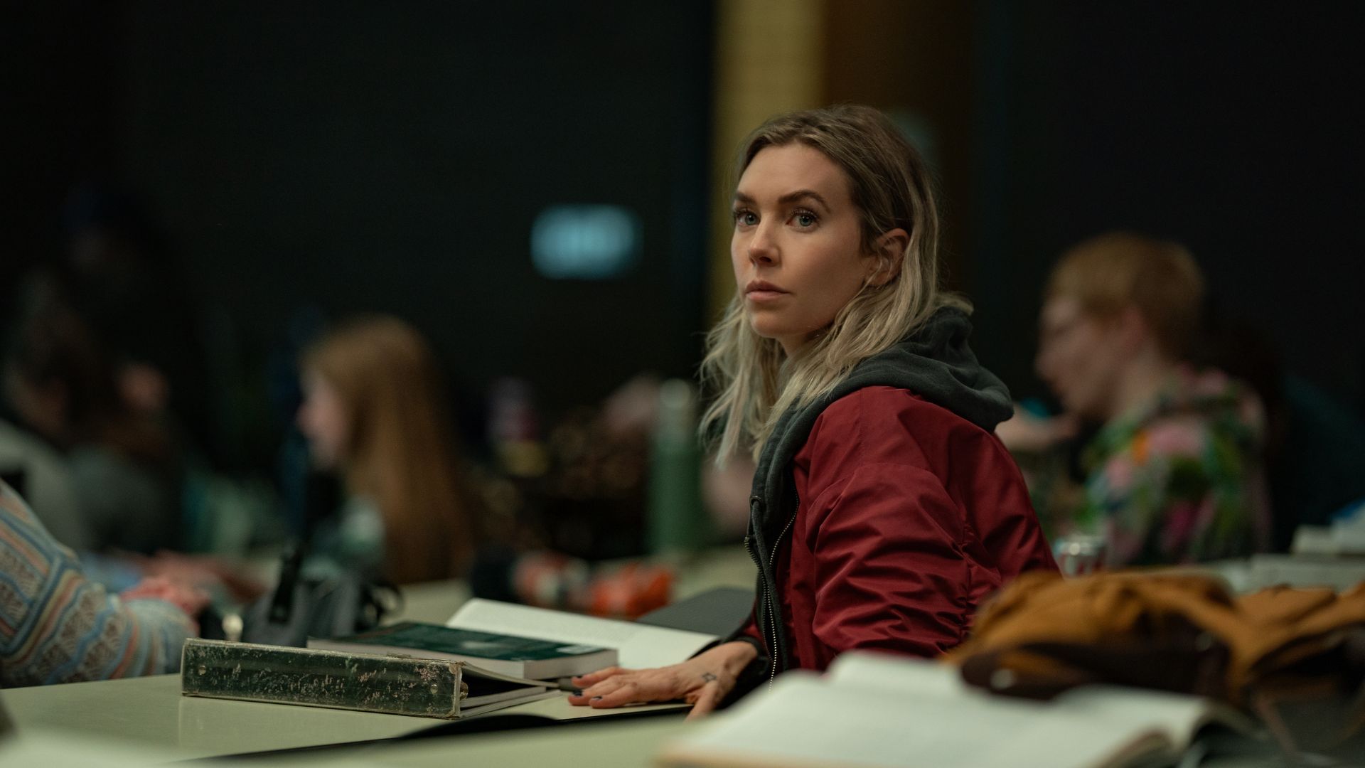 an image of Vanessa Kirby in night always changes, she is sitting at a desk in a building