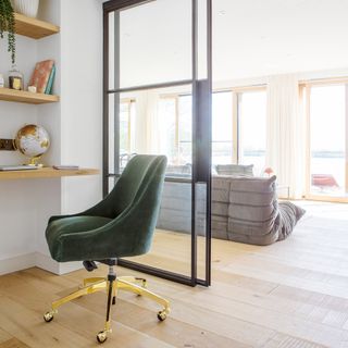 Home office with green velvet and brass swivel office chair and wooden shelf storage