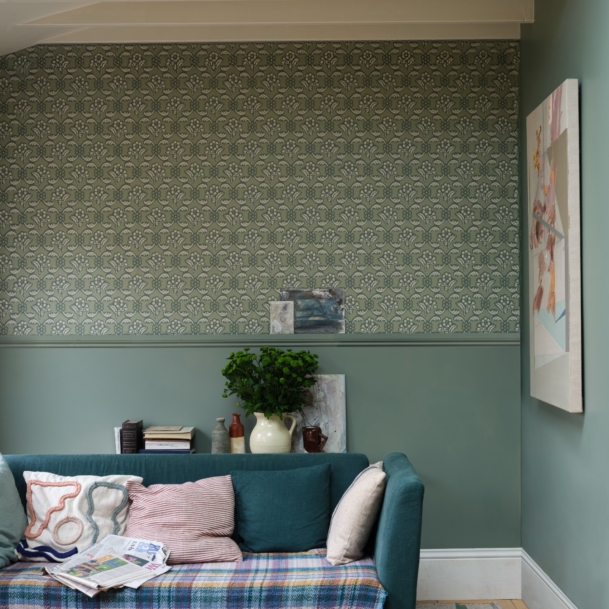 A small living room with a green sofa painted in Farrow & Ball's Card Room Green shade with a wallpapered panel