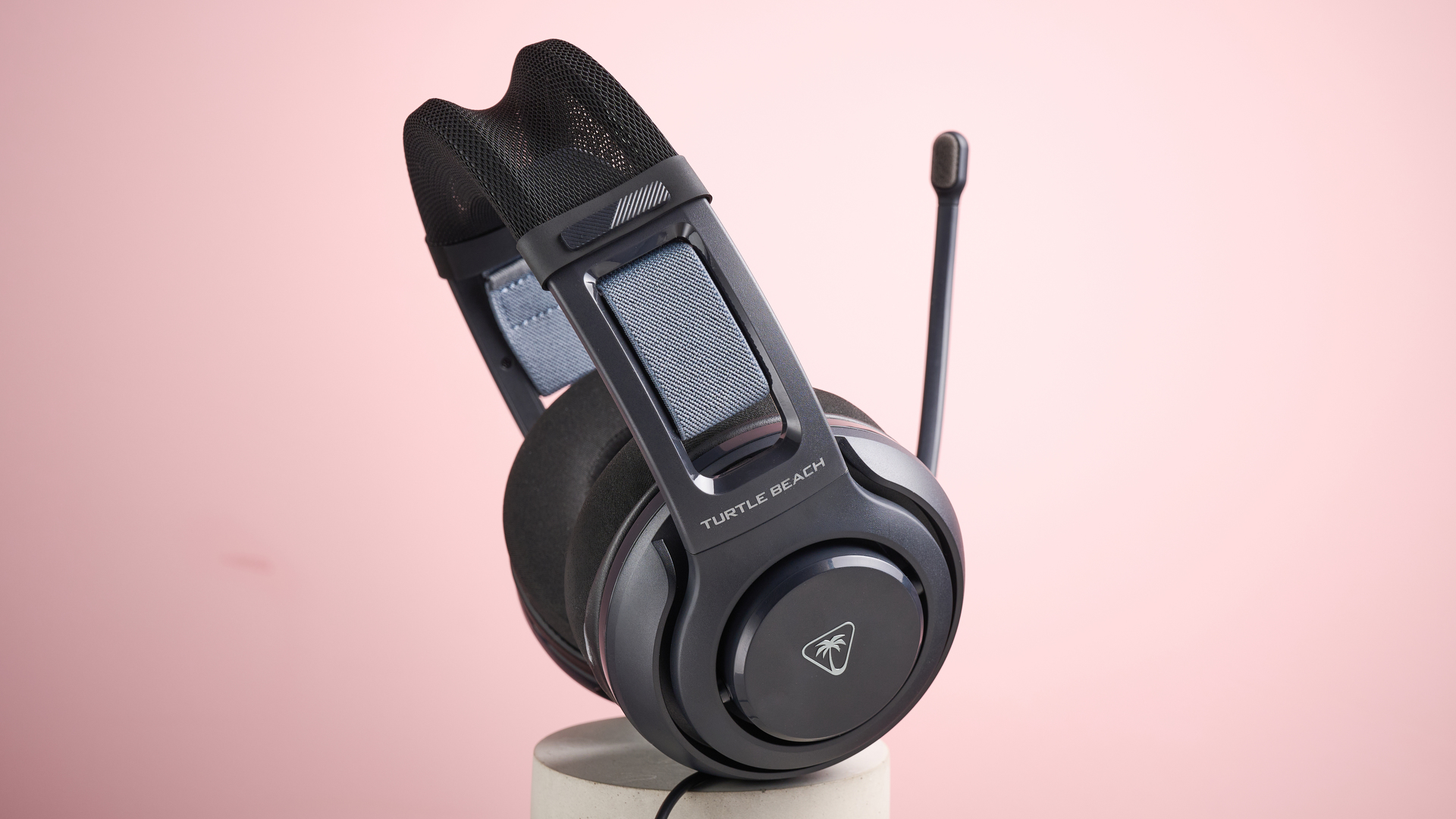 The Turtle Beach Atlas 200 sat on top of a cylinder, with the mic folded up, in front of a pink background.