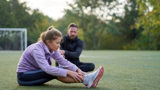 Woman stretching out hamstrings and legs with personal trainer in the park