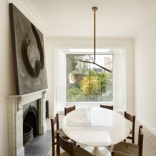 A minimalist dining room, with a large piece of art above a marble fireplace