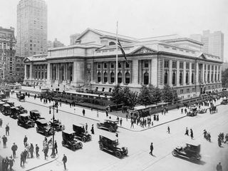 Pedestrian and automobile traffic crosses in front of the New York Public Library on July 14, 1915.