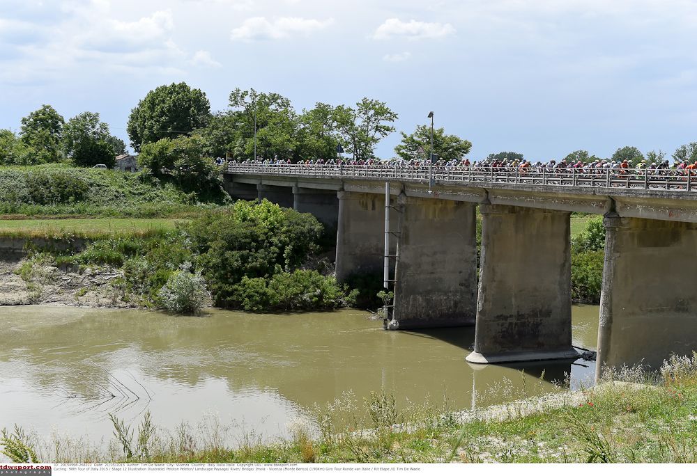 The peloton crosses a bridge in the Italian countryside.