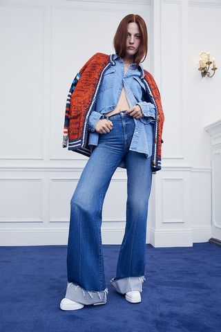 A model wearing blue cuffed jeans, denim shirt, red cardigan for MOTHER