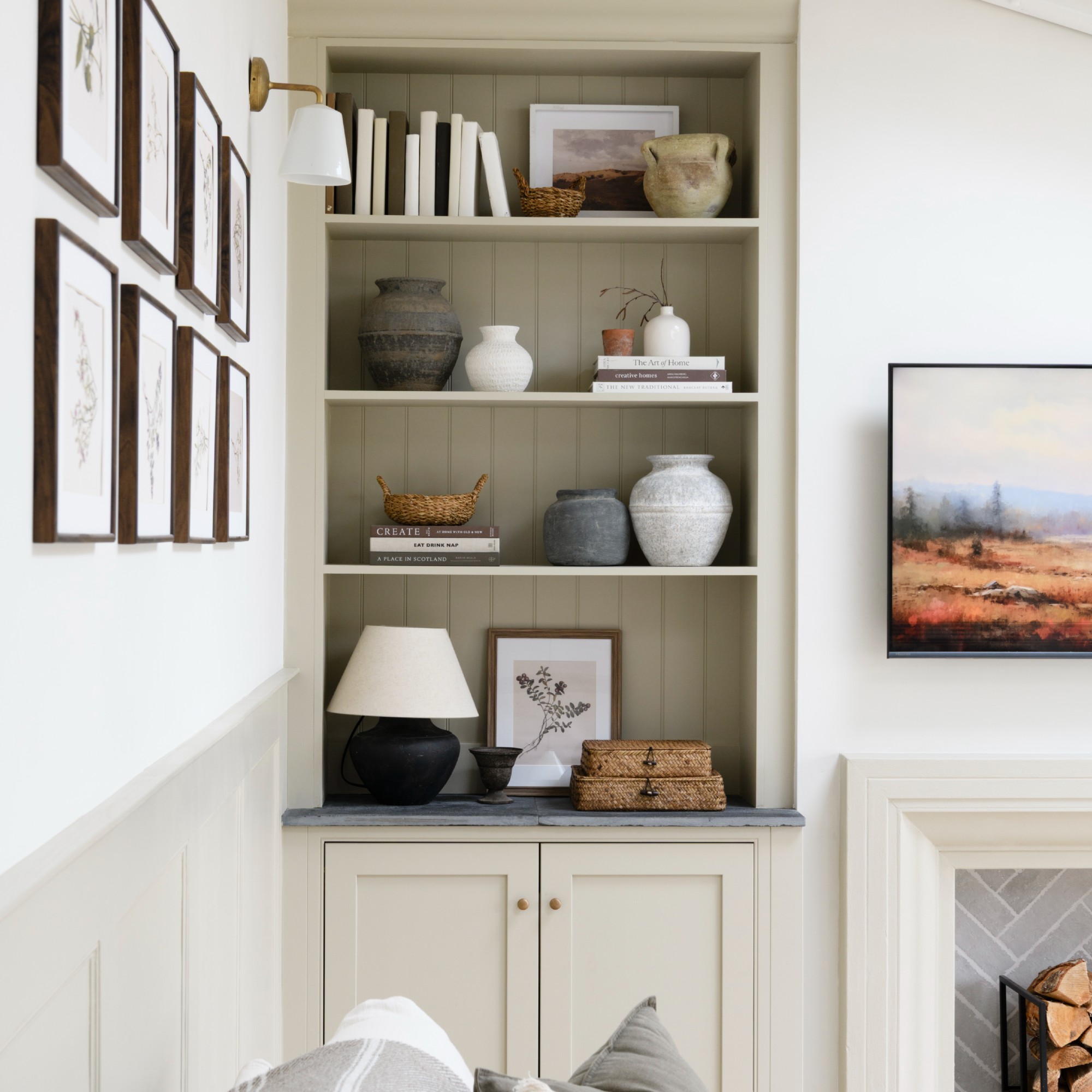 A light living room with a built-in bookcase into an alcove with a table lamp and a wall light