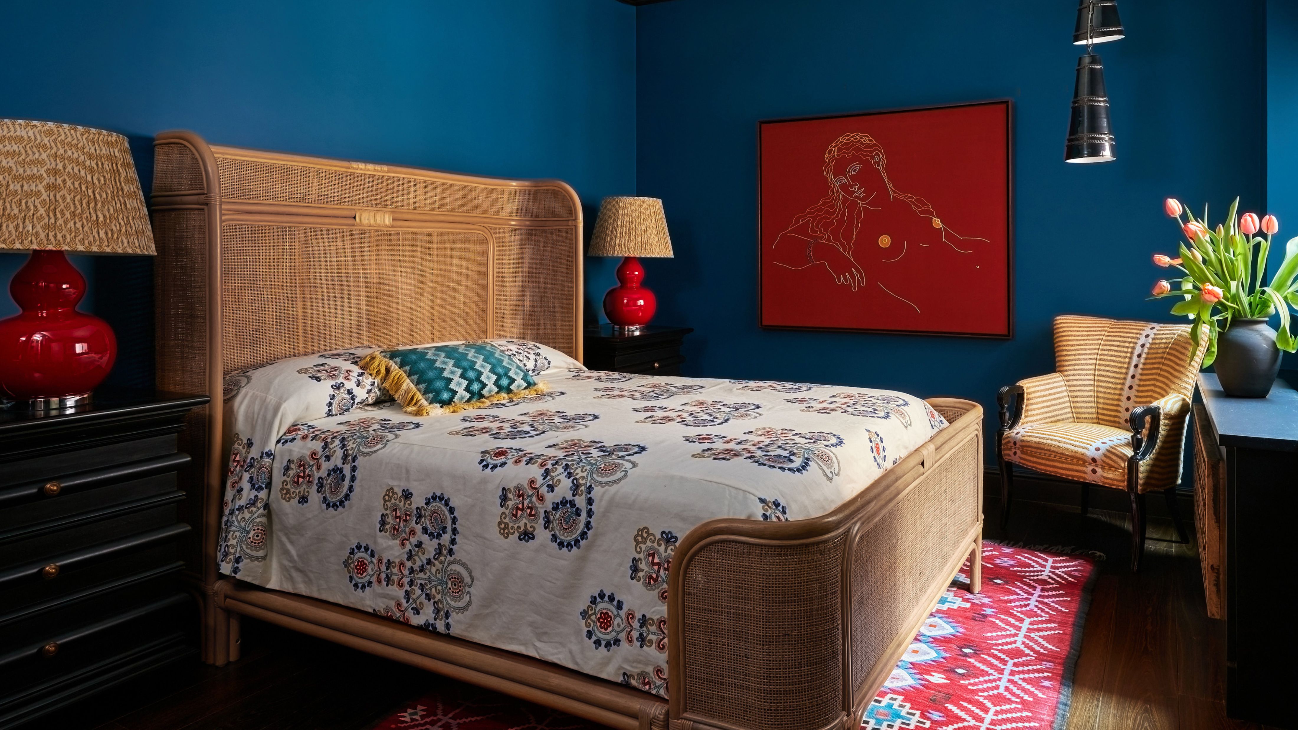 Eccentric Aunt-style bedroom featuring teal walls, a rattan bed frame, abstract art work, a patterned accent chair, and mismatched bedding